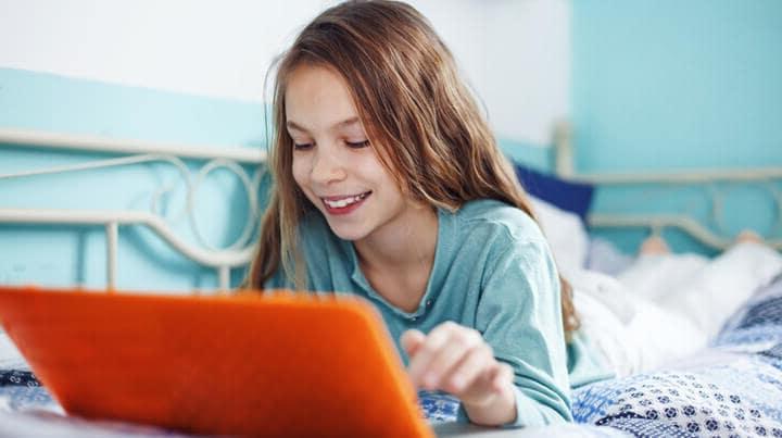 Girl laying on her bed looking at an orange laptop